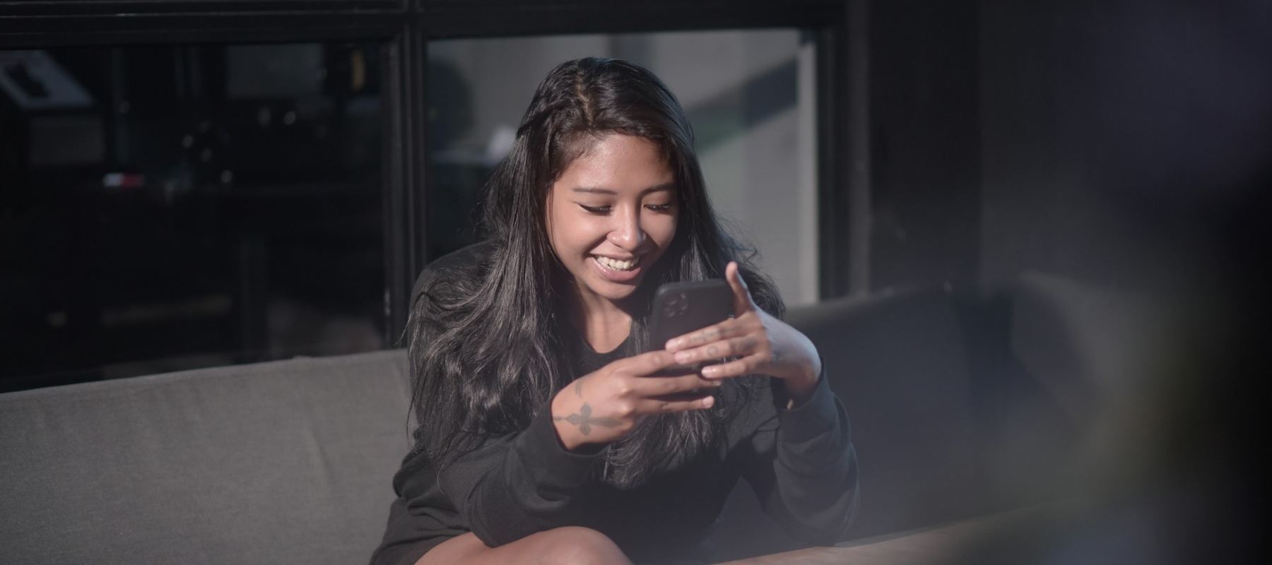 A woman smiling at her phone on her couch in the evening